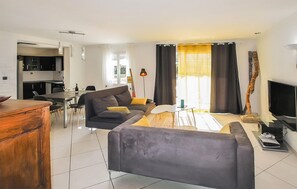A modern living room with a sofa, coffee table, and a TV. There is a dining area with a table and chairs. The room has a large window with curtains. - Stunning home in Espeluche with private swimming pool, can be inside or outside (Espeluche)
