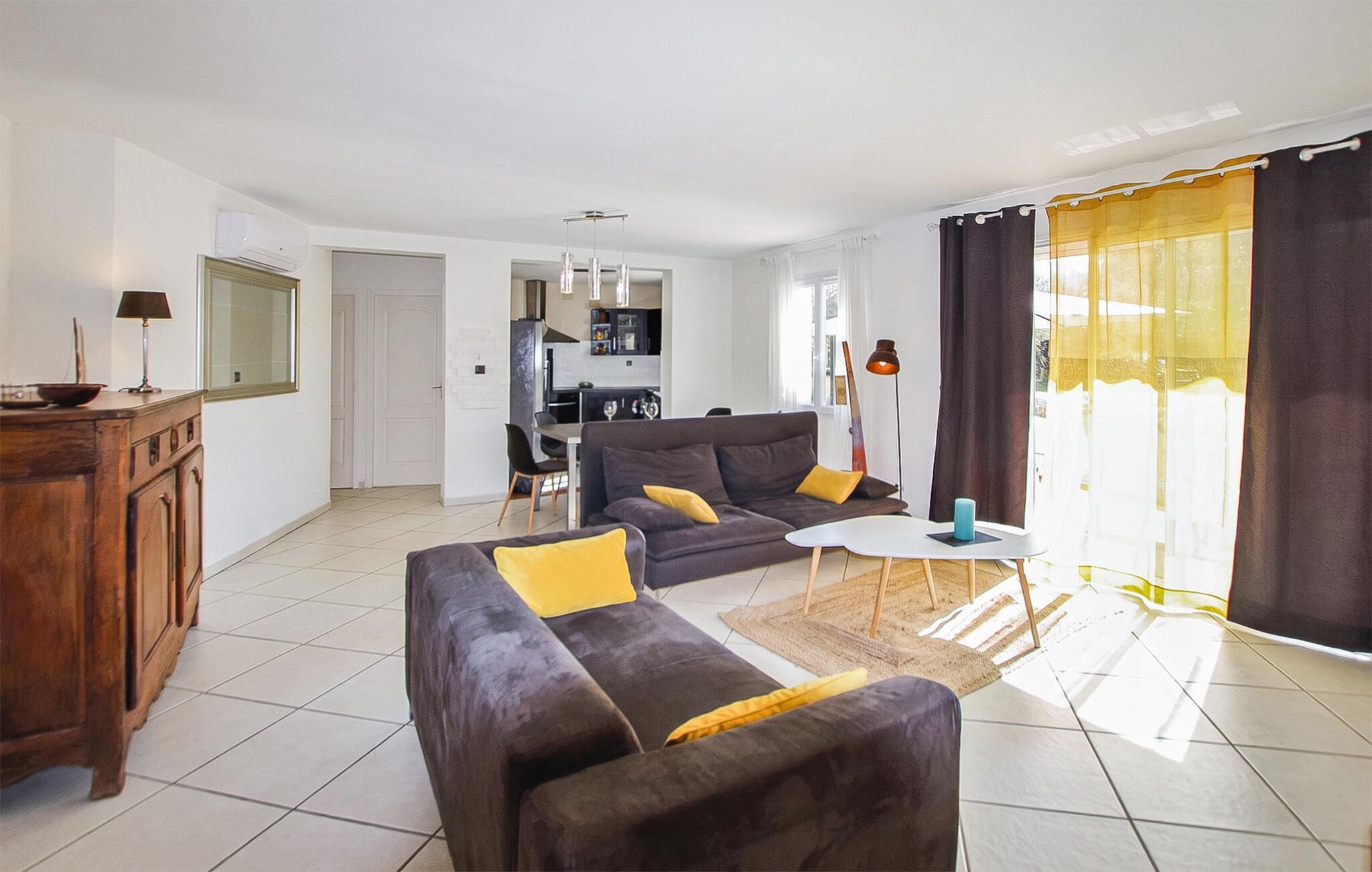 A living room with a sofa set, a dining area, and a kitchen in the background.