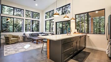 Eine moderne Küche mit großen Fenstern, einem Essbereich und einem Wohnraum mit Sofa und Couchtisch.