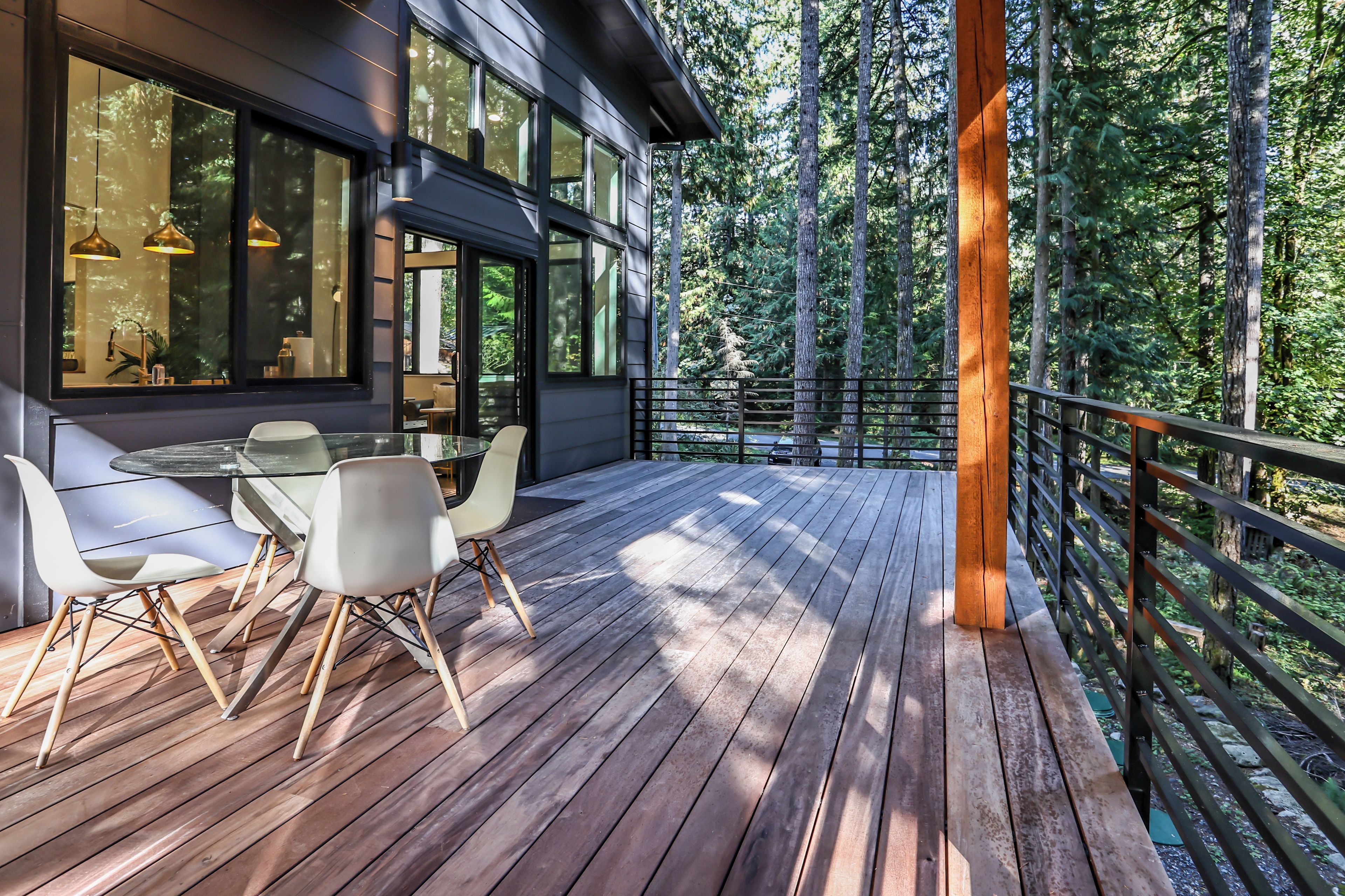 Une terrasse extérieure moderne, dotée d’un espace repas, et entourée d’une forêt.