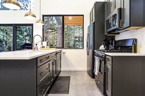 Een moderne keuken met een groot eiland, roestvrijstalen apparatuur en uitzicht op het bos.