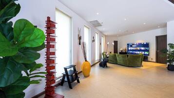 A modern hotel lobby with a reception desk, a large flat-screen TV displaying various channels, and a green sofa.
