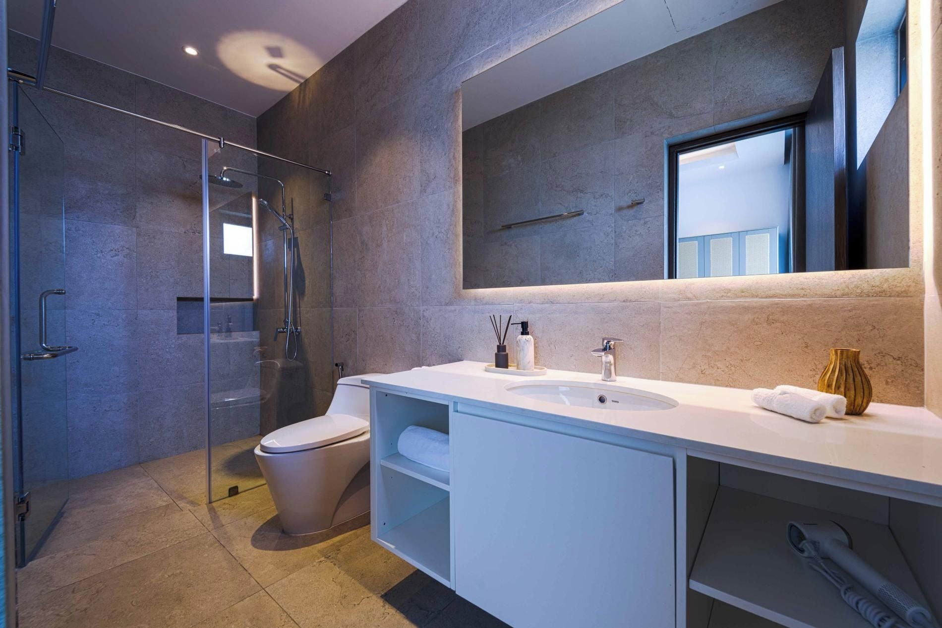 A modern bathroom with a glass shower enclosure, a toilet, a white vanity with a mirror, and a sink.