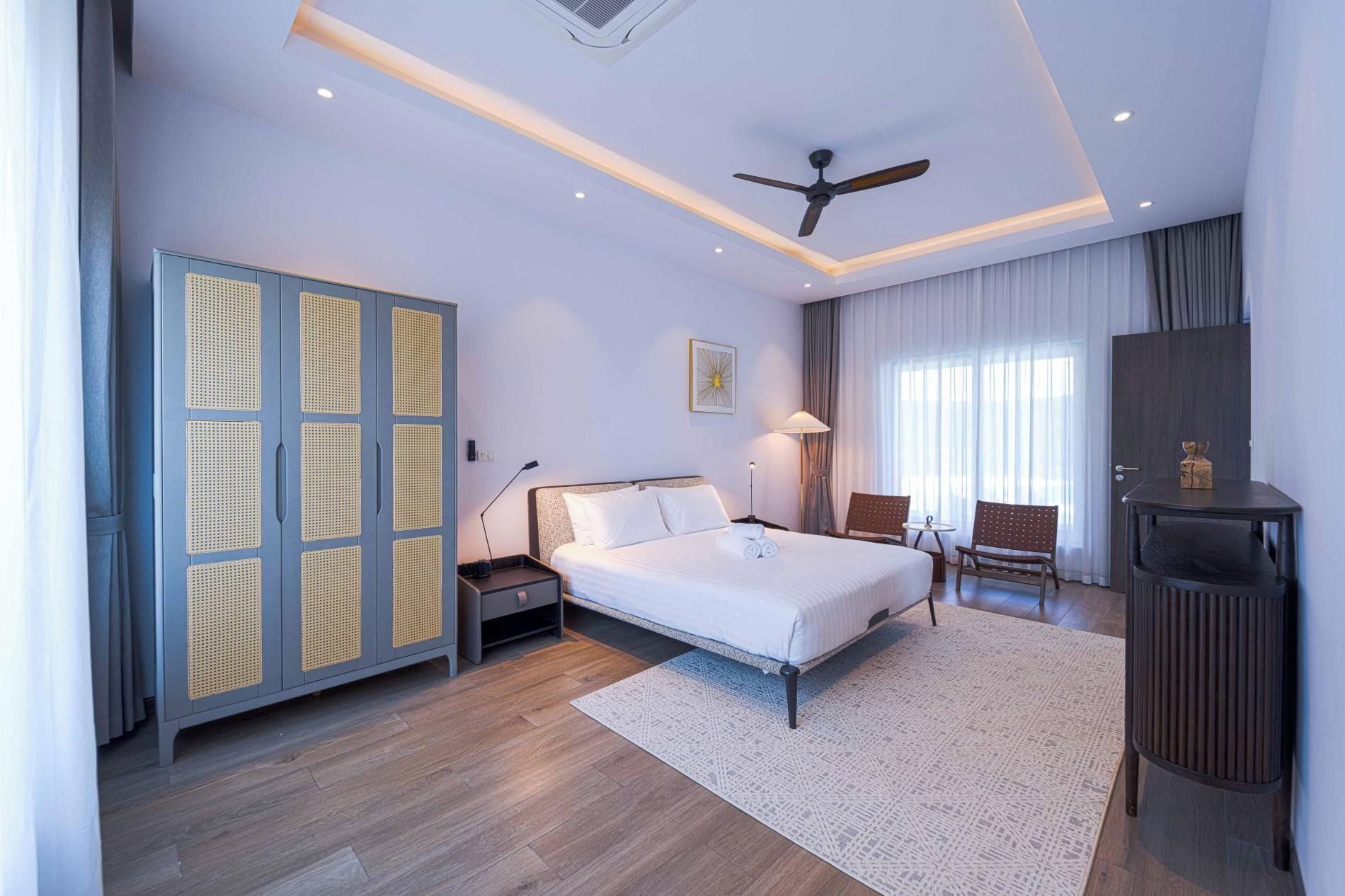 A modern hotel room with a large bed, a desk, a chair, a wardrobe, and a ceiling fan.