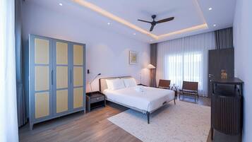 A modern hotel room with a large bed, a desk, a chair, a wardrobe, and a ceiling fan.