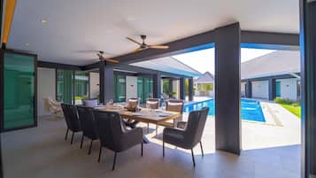 A spacious outdoor dining area with a pool, modern furniture, and a view of the surrounding landscape.