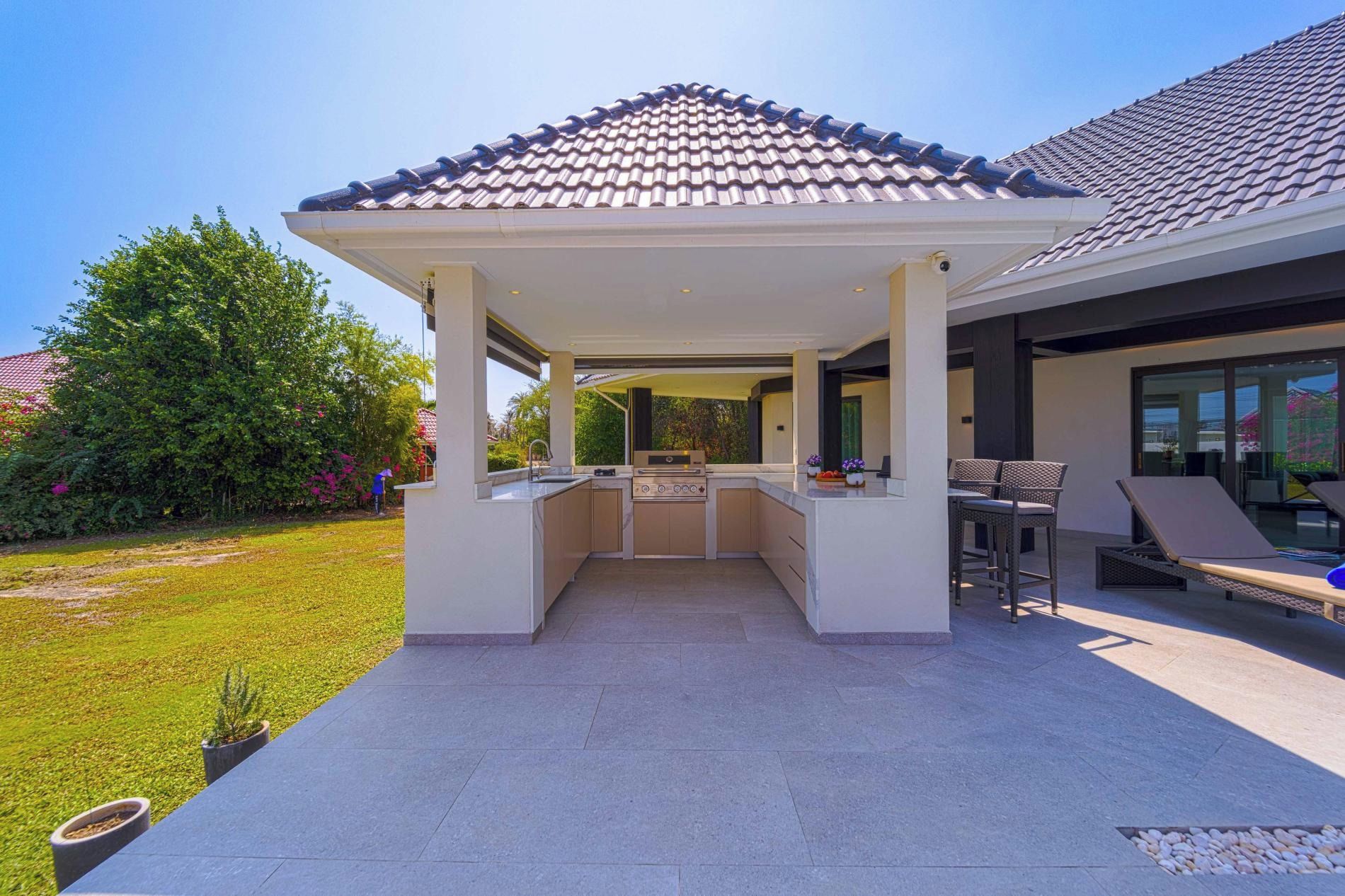 A covered outdoor kitchen area with a gas stove, bar stools, and a pergola.