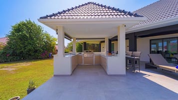 A covered outdoor kitchen area with a gas stove, bar stools, and a pergola.