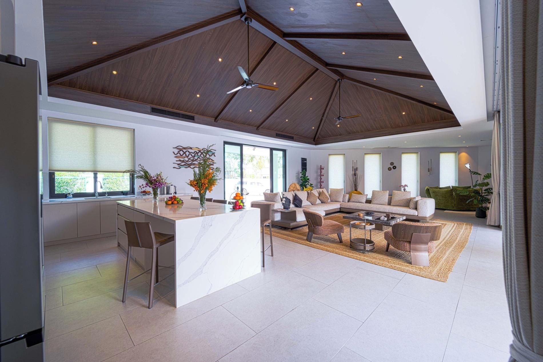 A spacious living area with a large island, seating arrangements, and a high ceiling with exposed beams.