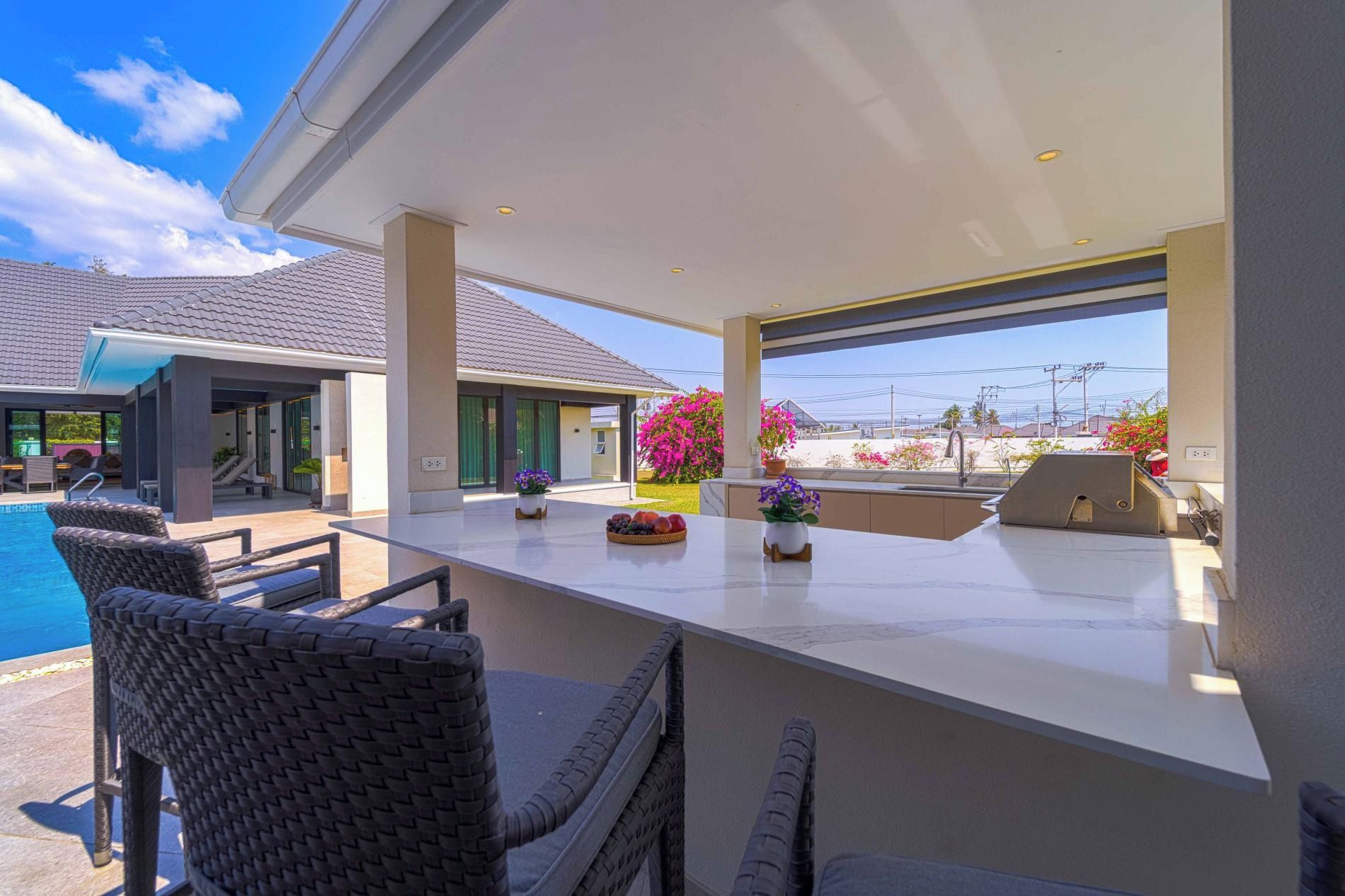 A modern outdoor kitchen area with a pool, outdoor seating, and a view of the surrounding landscape.