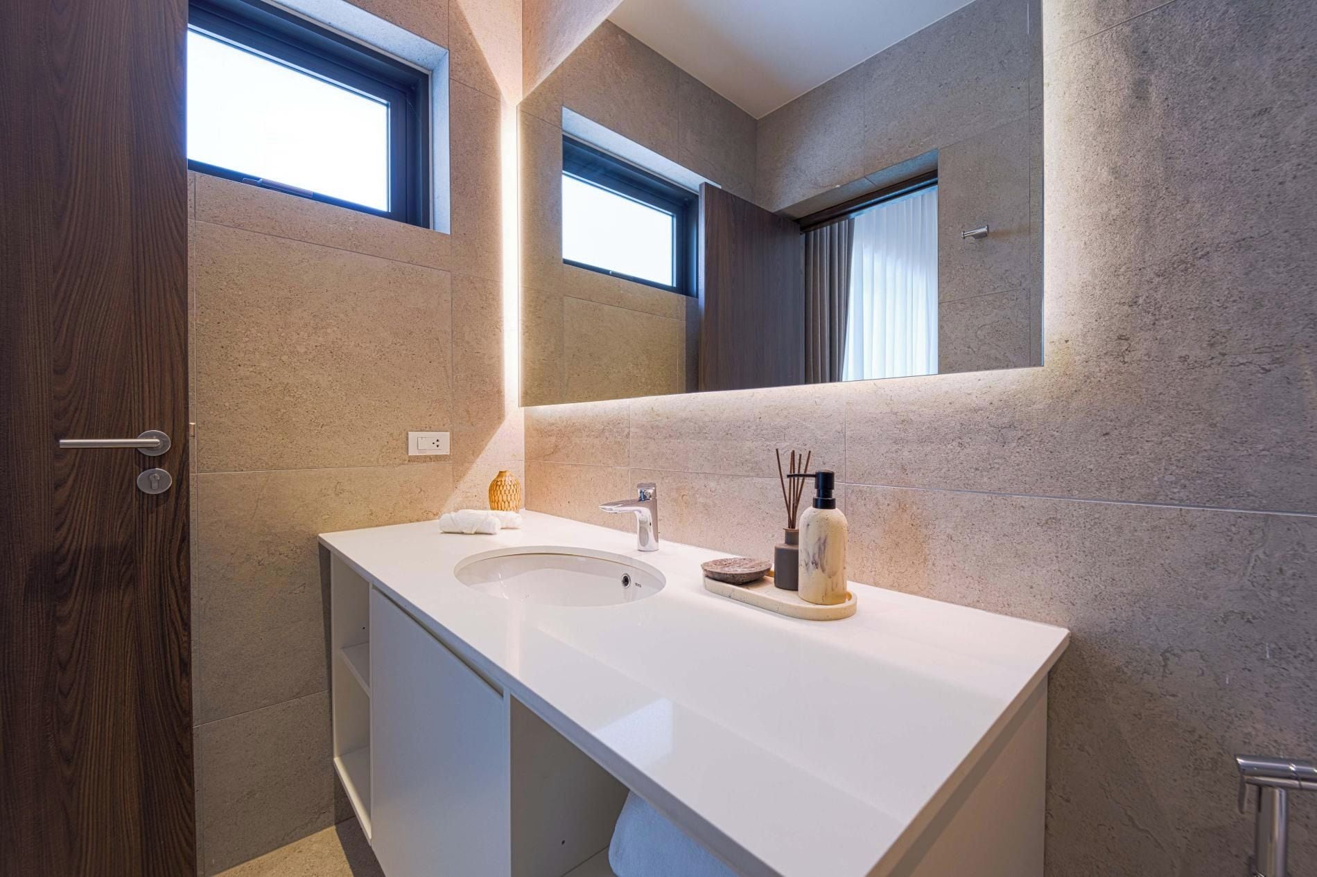 A modern bathroom with a white vanity, a large mirror, and a window.