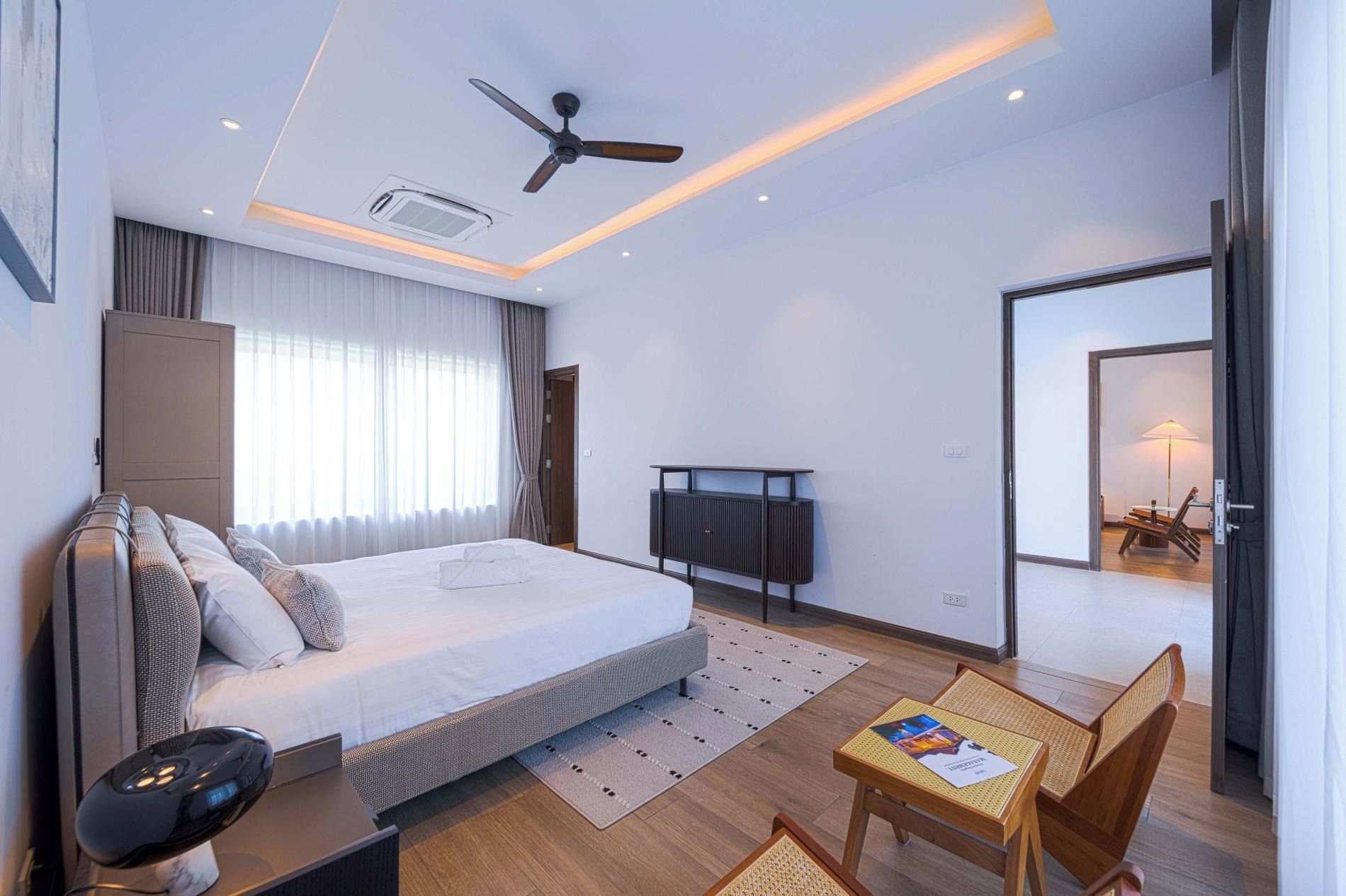 A modern hotel room with a bed, a desk, a chair, a ceiling fan, and a television.