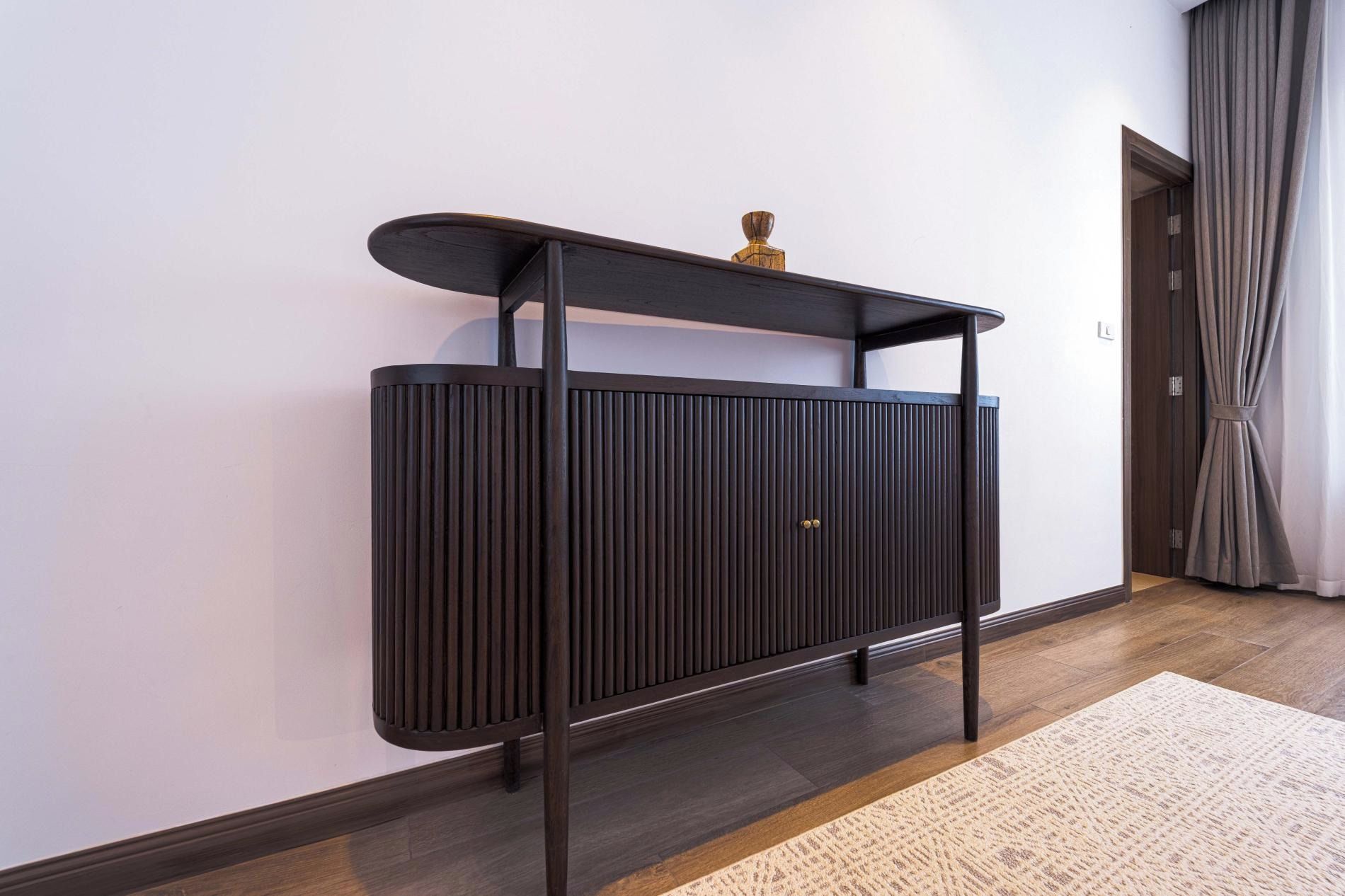 A dark wooden console table with a shelf, a decorative item on top, and a textured rug on the floor.