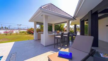 An outdoor patio with a covered seating area, a grill, and a pool.