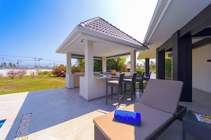 An outdoor patio with a covered seating area, a grill, and a pool.
