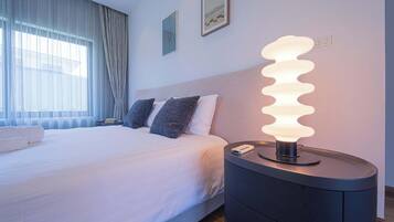 Quarto de hotel com cama, mesa de cabeceira com abajur e janela com cortinas.