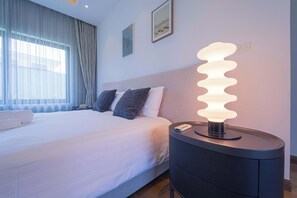 Una habitación de hotel con una cama, una mesita de noche con lámpara y una ventana con cortinas.