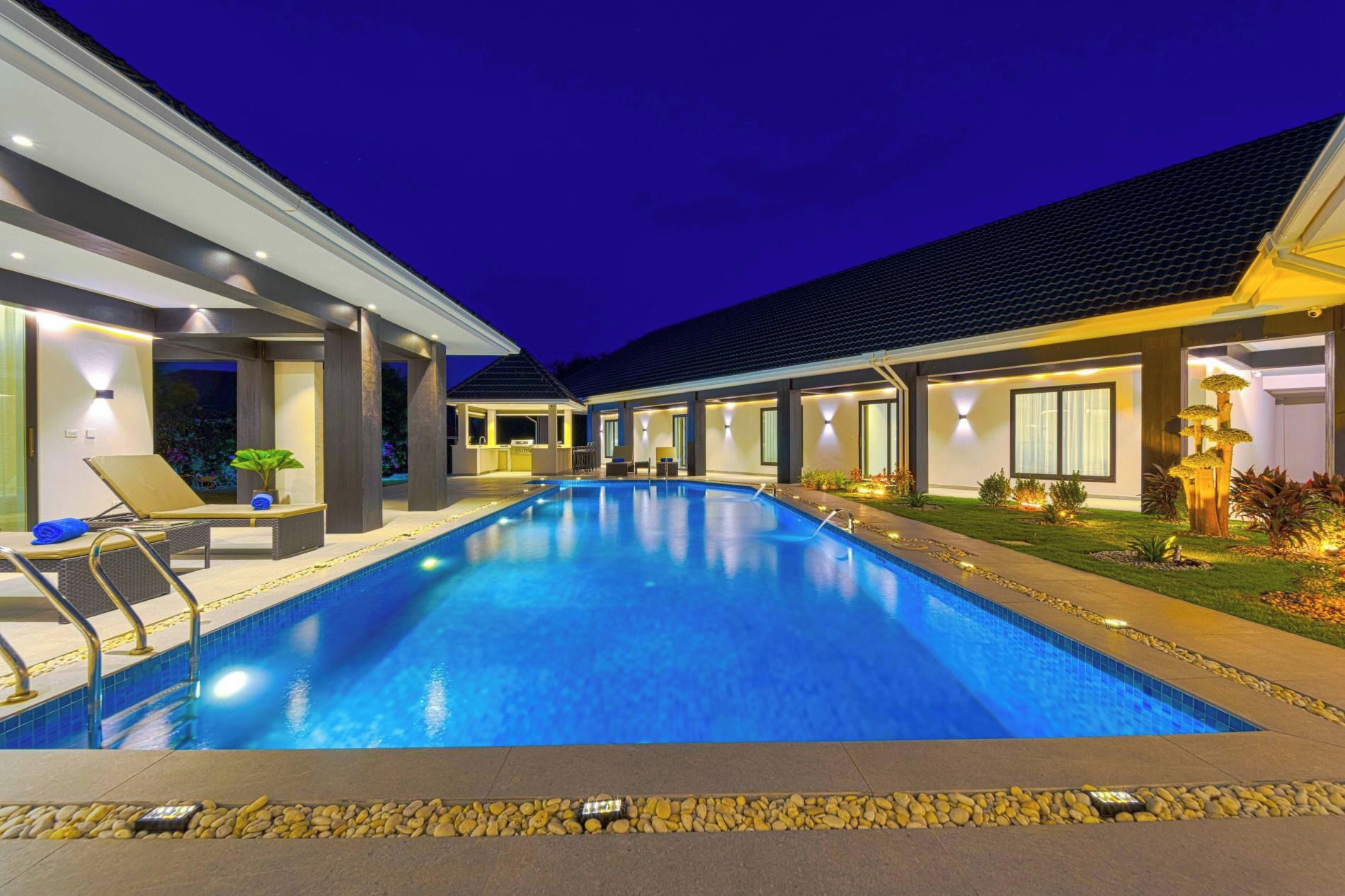A modern hotel with a swimming pool, lounge chairs, and a well-lit outdoor area.