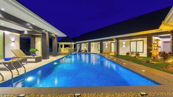 A modern hotel with a swimming pool, lounge chairs, and a well-lit outdoor area.