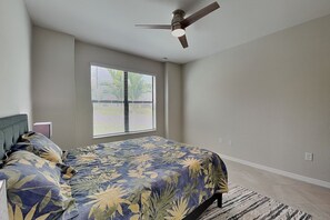 Ein Schlafzimmer mit einem Bett, einem Deckenventilator, einem Fenster mit Jalousien und einem Teppich.