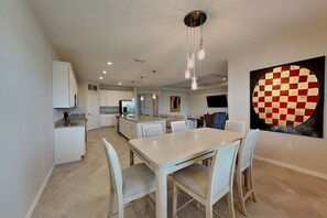A modern kitchen with white cabinetry, a dining area with a light-colored table and chairs, and a large abstract painting on the wall. - The Nomeblla Oasis (Fort Myers)