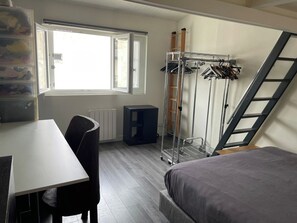 A bedroom with a bed, a desk, a chair, a radiator, a window, a clothes rack, and a ladder. - Designer apartment in the middle of Paris (Paris)