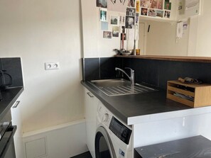 Cuina compacta amb rentadora integrada, un rentapeus i un moble d'emmagatzematge de fusta.