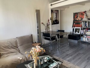Un saló modern amb un sofà, una taula de centre amb un vas, una taula de menjador amb cadires, i una biblioteca.