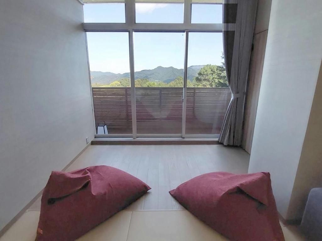 A room with a large window, two red cushions on the floor, and a view of mountains.
