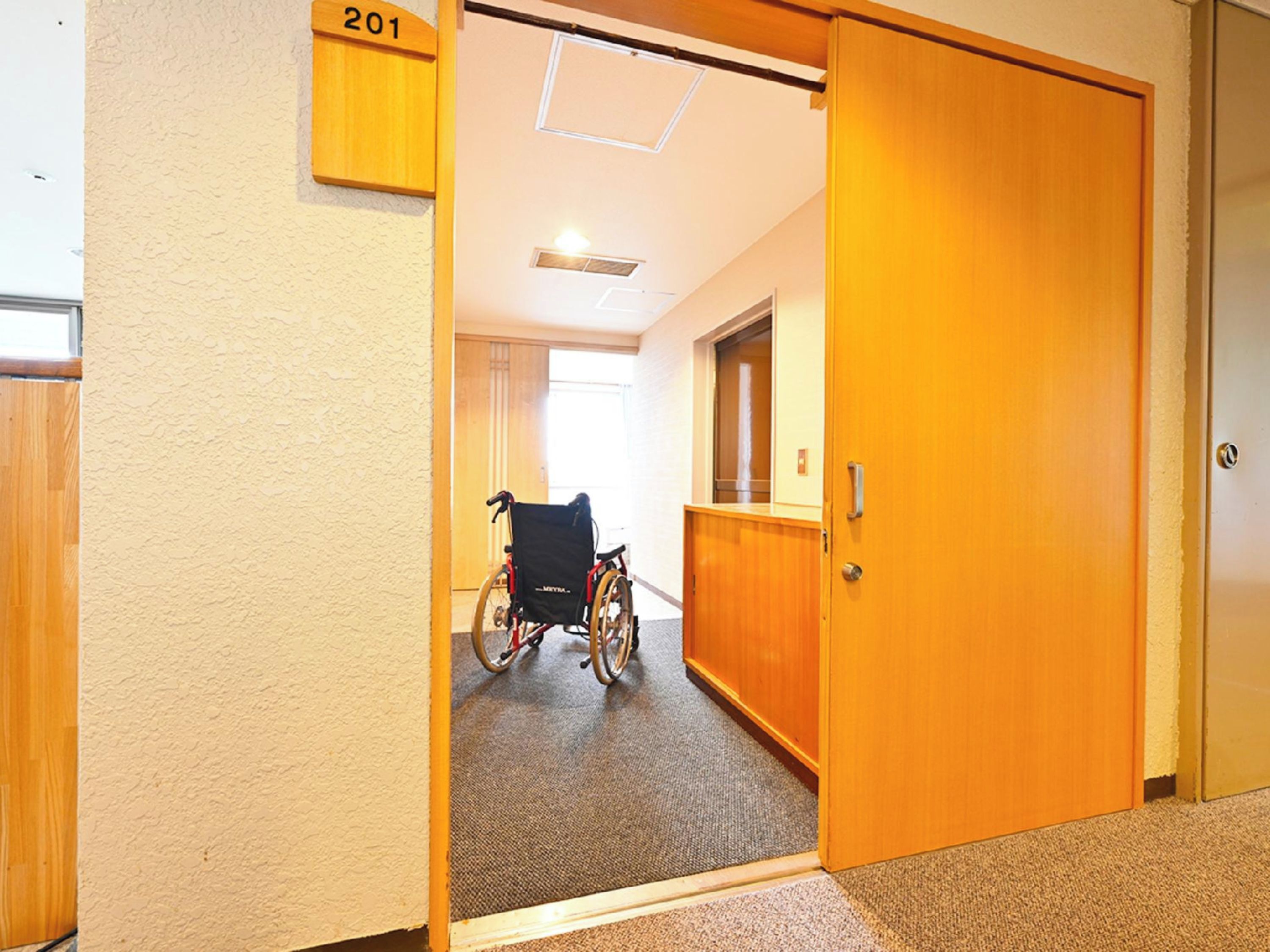 A wheelchair in a hallway with a door labeled '201' and a carpeted floor.