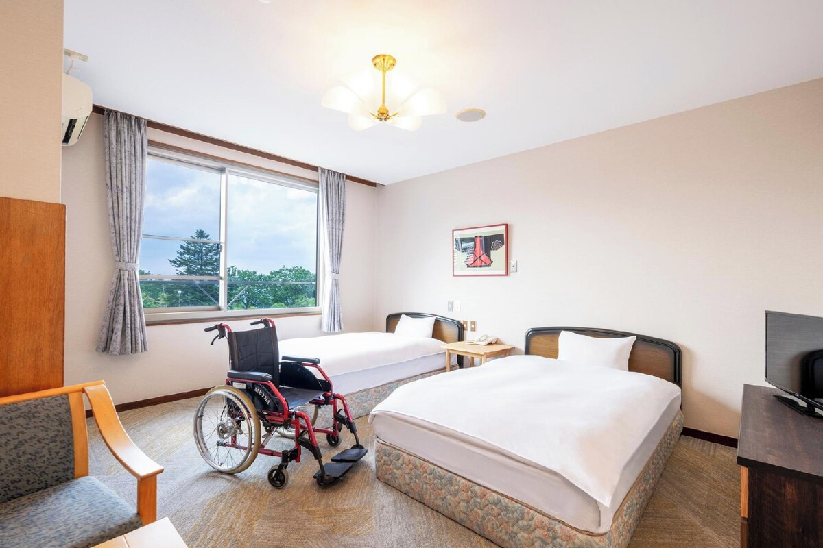 Habitación de hotel con silla de ruedas, cama, escritorio y televisor.