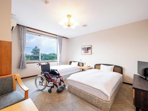 Habitación de hotel con silla de ruedas, cama, escritorio y televisor.
