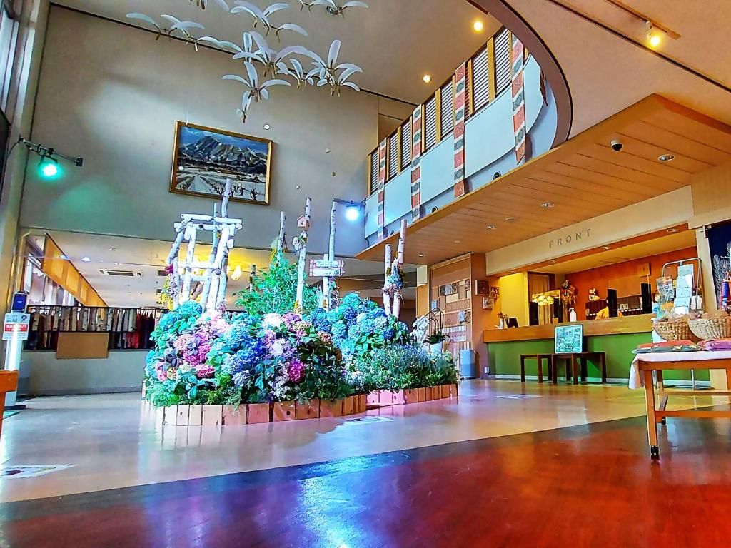 A lobby with a central floral arrangement, a reception desk, and a staircase leading to an upper level.
