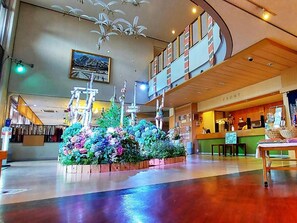 A lobby with a central floral arrangement, a reception desk, and a staircase leading to an upper level. - Ikoinomura Heritage Minoyama (Minano)