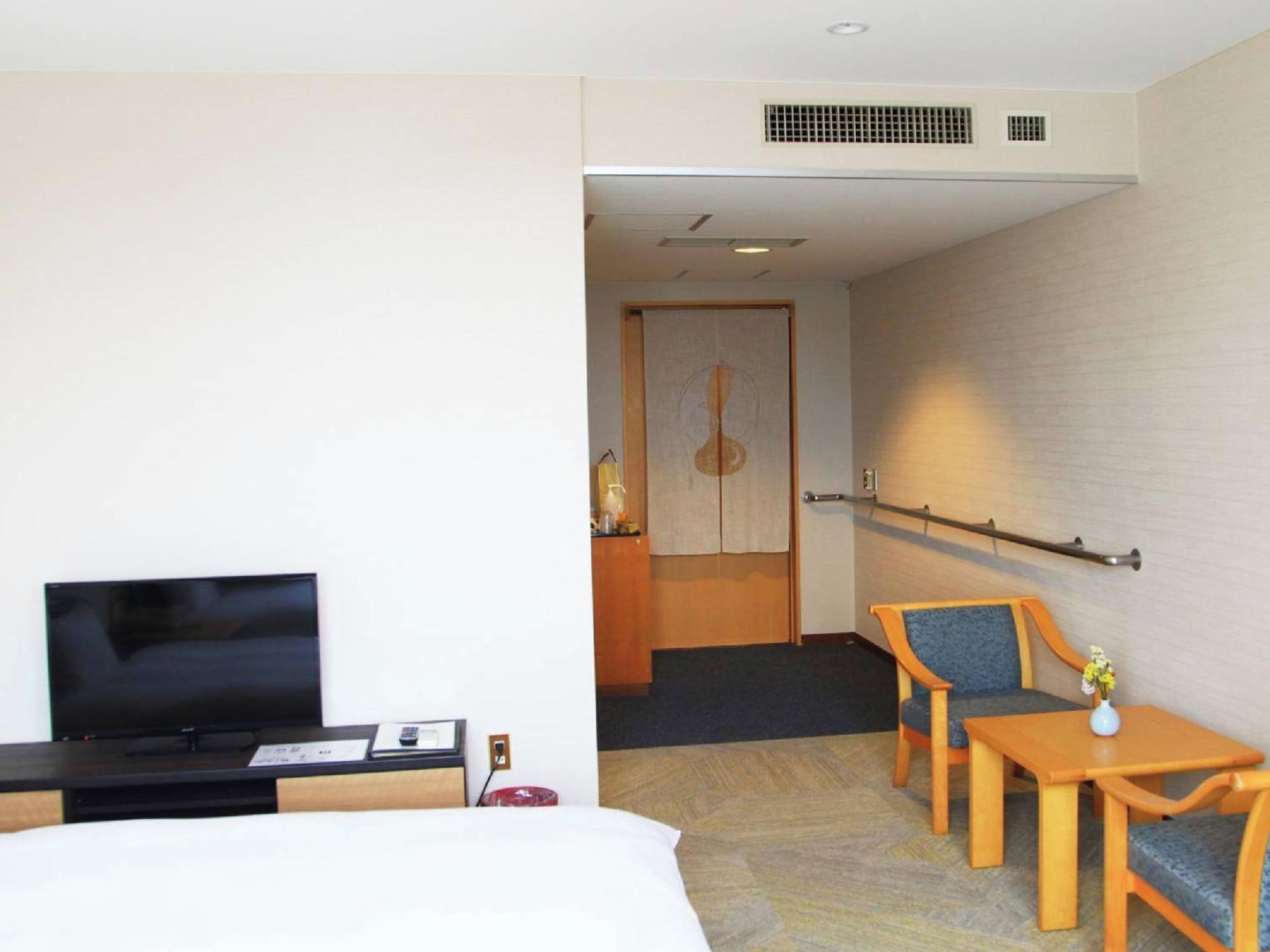 A hotel room with a bed, a television, a desk, a chair, and a small table with a vase.