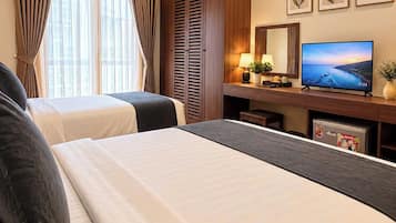 Quarto de hotel com duas camas, televisão, escrivaninha com luminária e janela com cortinas.