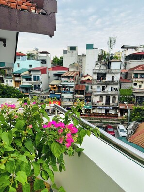 Uma varanda com vista para uma área urbana densamente povoada, mostrando diversos edifícios e uma rua com carros estacionados.