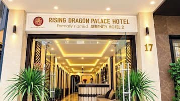Entrada do Hotel Rising Dragon Palace, com balcão de recepção, plantas em vasos e vista clara para o interior.