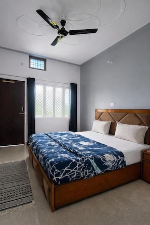 A bedroom with a bed, a ceiling fan, a window with curtains, and a door. - Himalayan Nest Chopta (Ukhimath)
