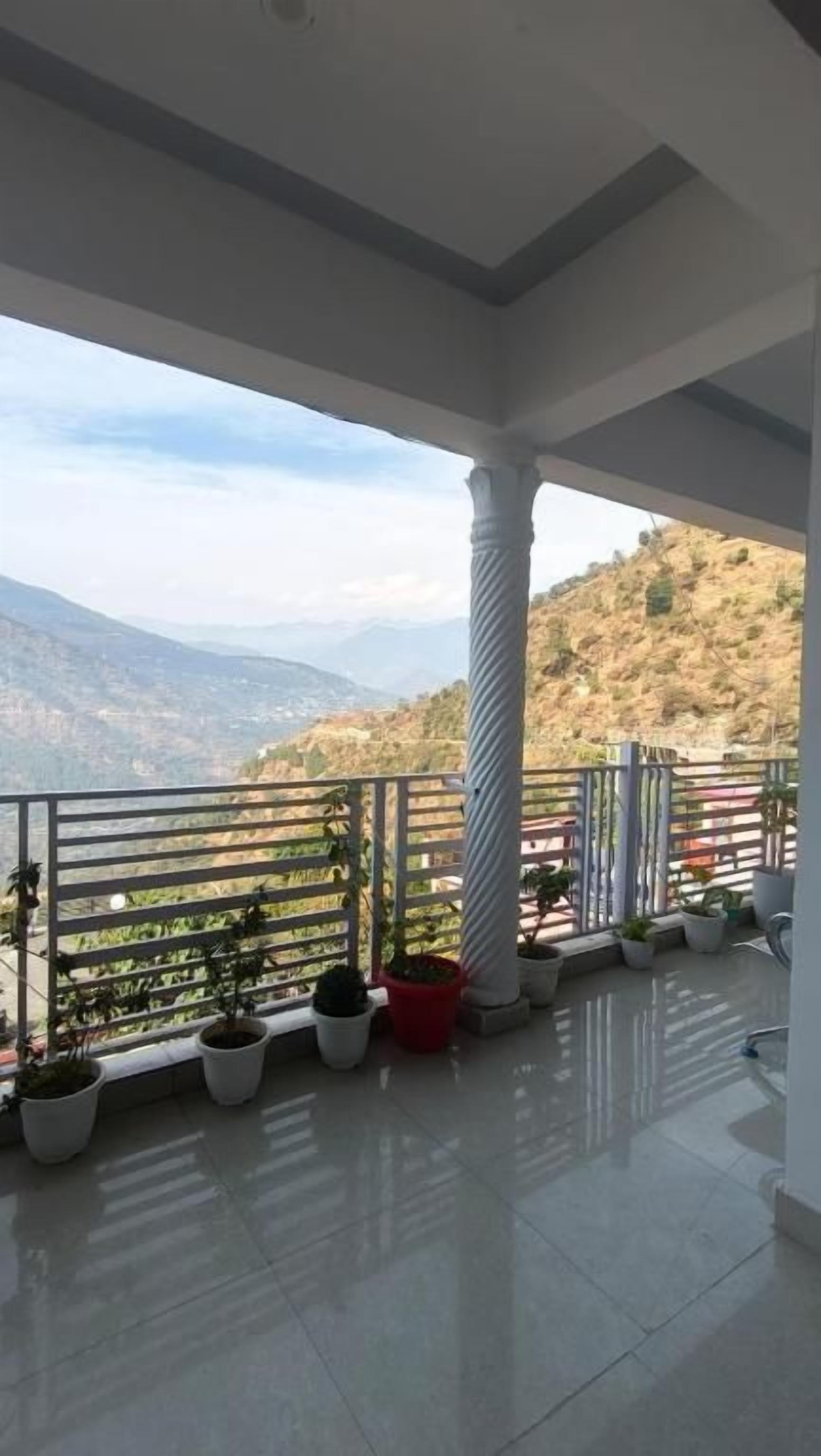 Un balcón con vistas a montañas, plantas en macetas y una barandilla.