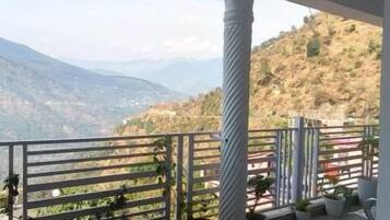 Un balcón con vistas a montañas, plantas en macetas y una barandilla.