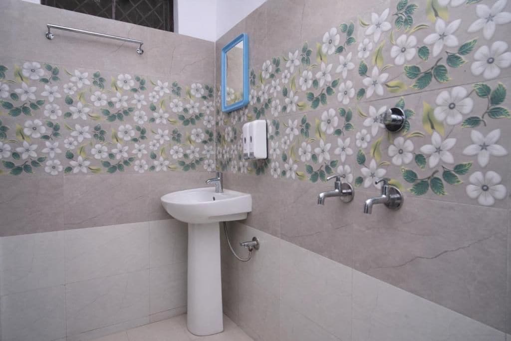 Un baño con un lavamanos pedestal blanco, un espejo y una pared con un diseño de azulejos florales.