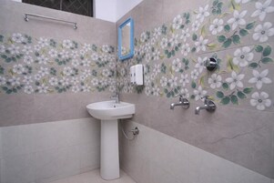 A bathroom with a white pedestal sink, a mirror, and a wall with a floral tile pattern.