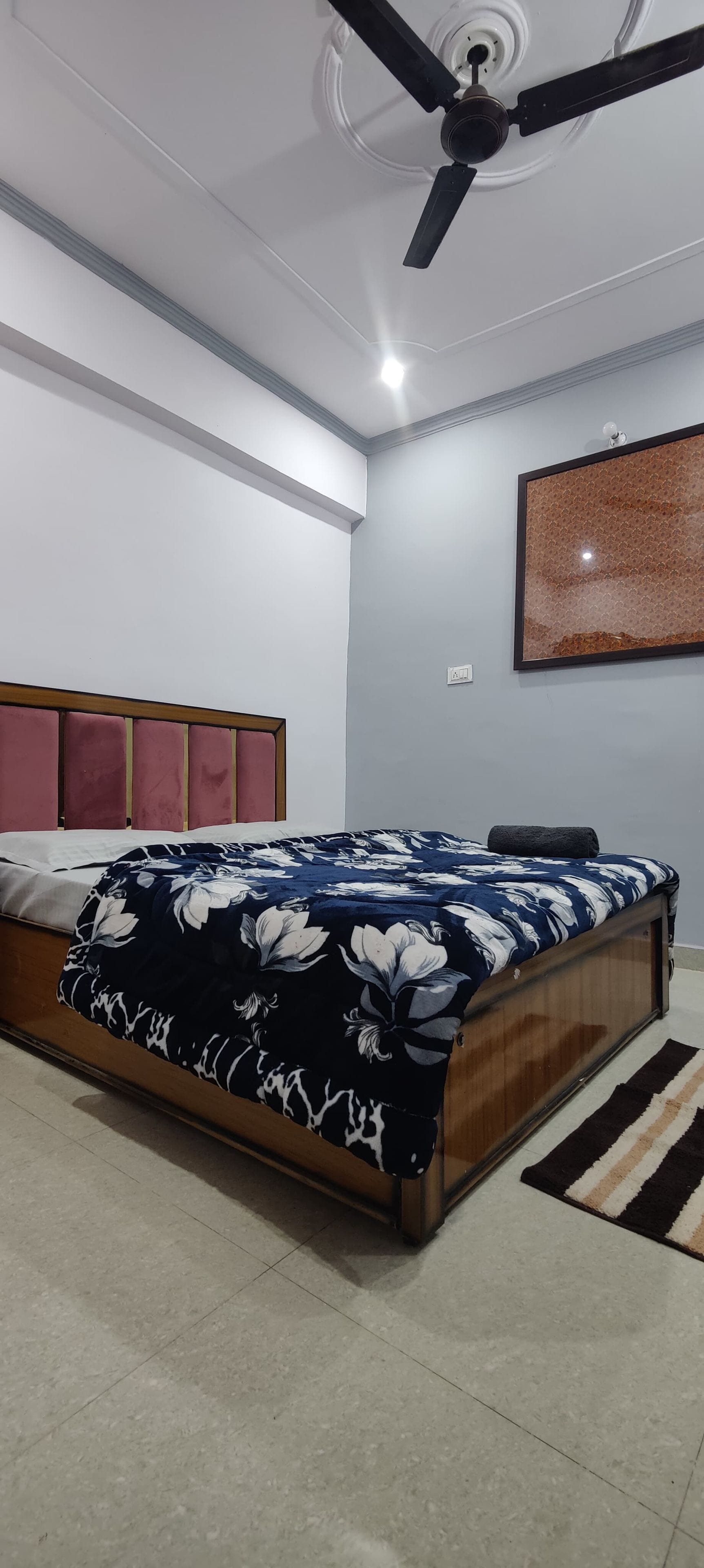 Une chambre à coucher avec un lit, un ventilateur de plafond, une lampe fixée au mur et un tableau encadré.