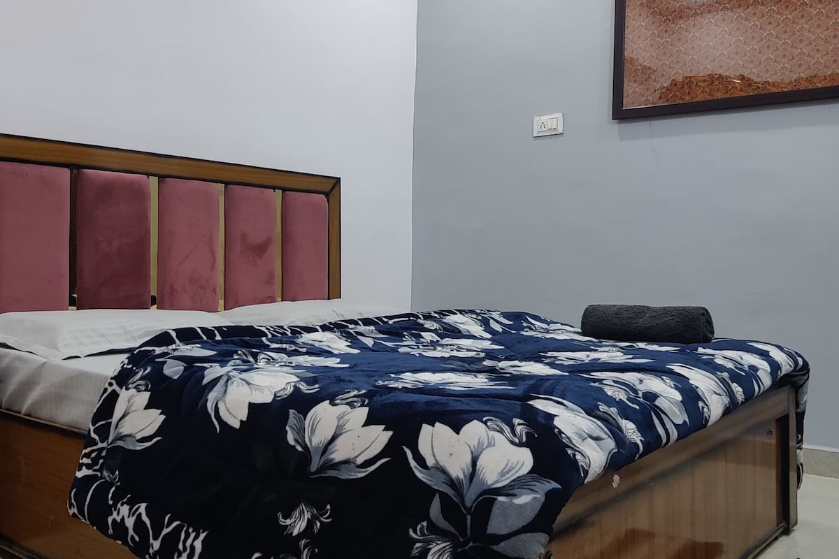 A bedroom with a bed, a ceiling fan, a wall-mounted light, and a framed picture.