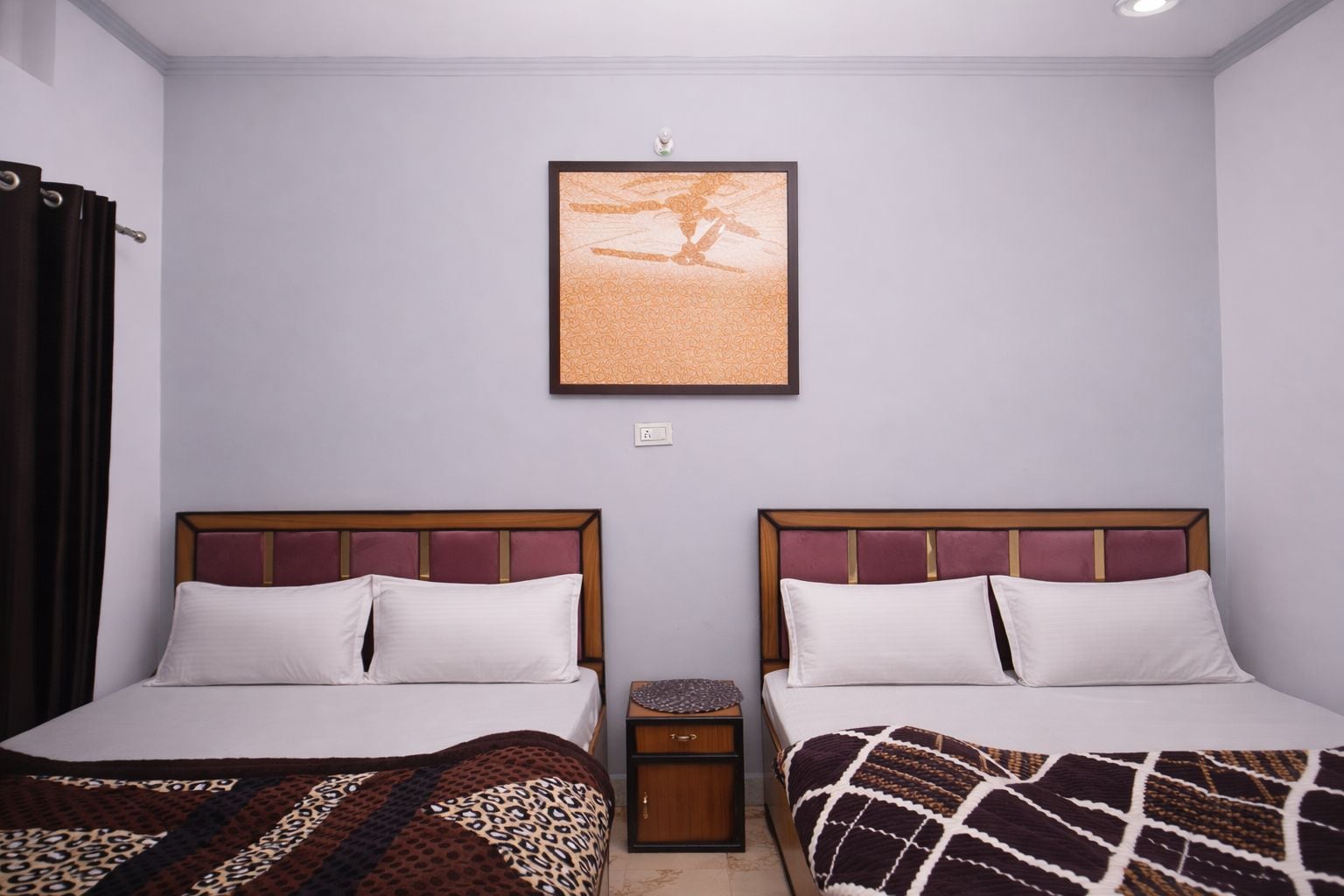 Habitación de hotel con dos camas, una mesita de noche, un cuadro enmarcado en la pared y una ventana con cortinas.