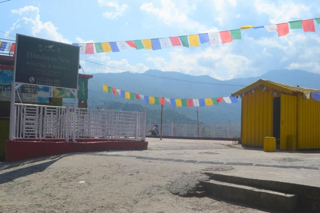 Un hostal llamado Himalayan Nest, con un letrero, un área cercada y un edificio amarillo al fondo.
