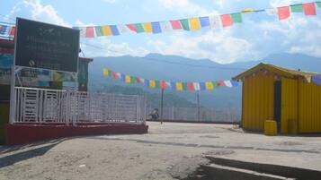 Un hostal llamado Himalayan Nest, con un letrero, un área cercada y un edificio amarillo al fondo.