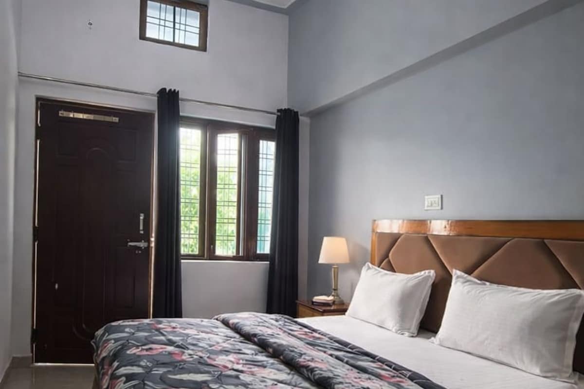 A bedroom with a bed, a nightstand, a ceiling fan, a window with curtains, and a door.