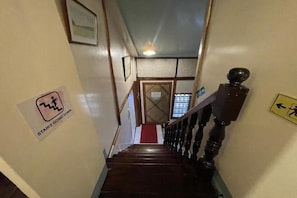 A wooden staircase with a red carpet leading to a door. There are signs on the walls, one indicating 'stairs going down' and another with a directional arrow.